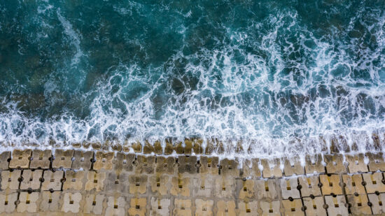 Emerald waves washing off the seawall constructed of small cubical concrete structures