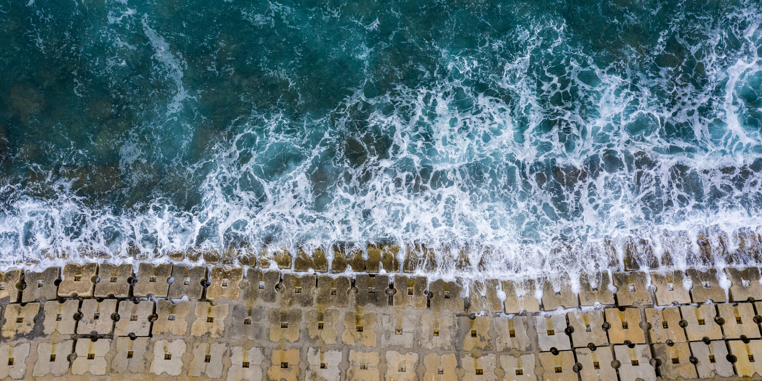 Emerald waves washing off the seawall constructed of small cubical concrete structures